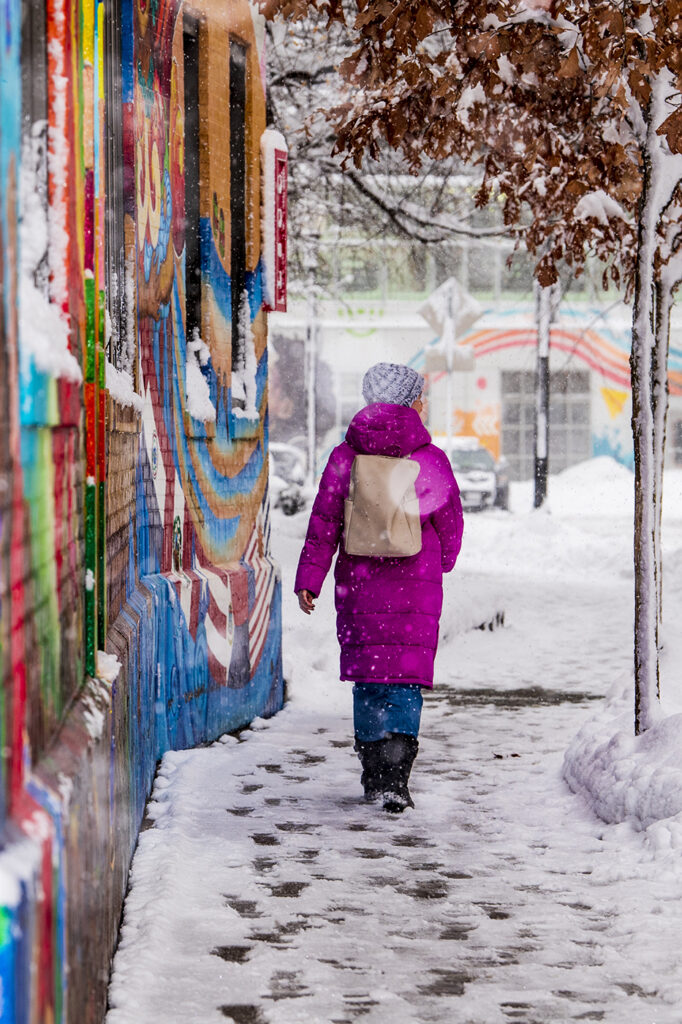 A student walking down a snowy sidewalk past a colorful mural.