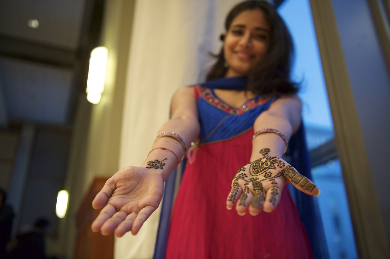 A female student poses with hands held out, showing the henna designs on the palms of her hands to the camera.