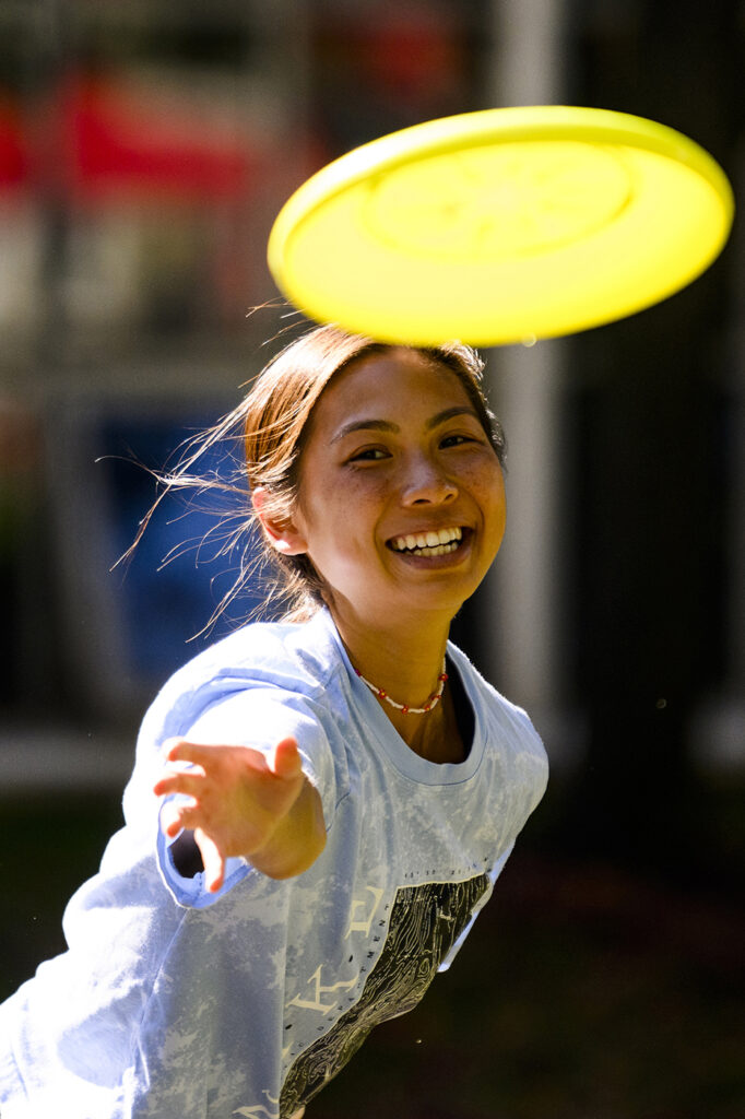 A student smiling and throwing a yellow frisbee.