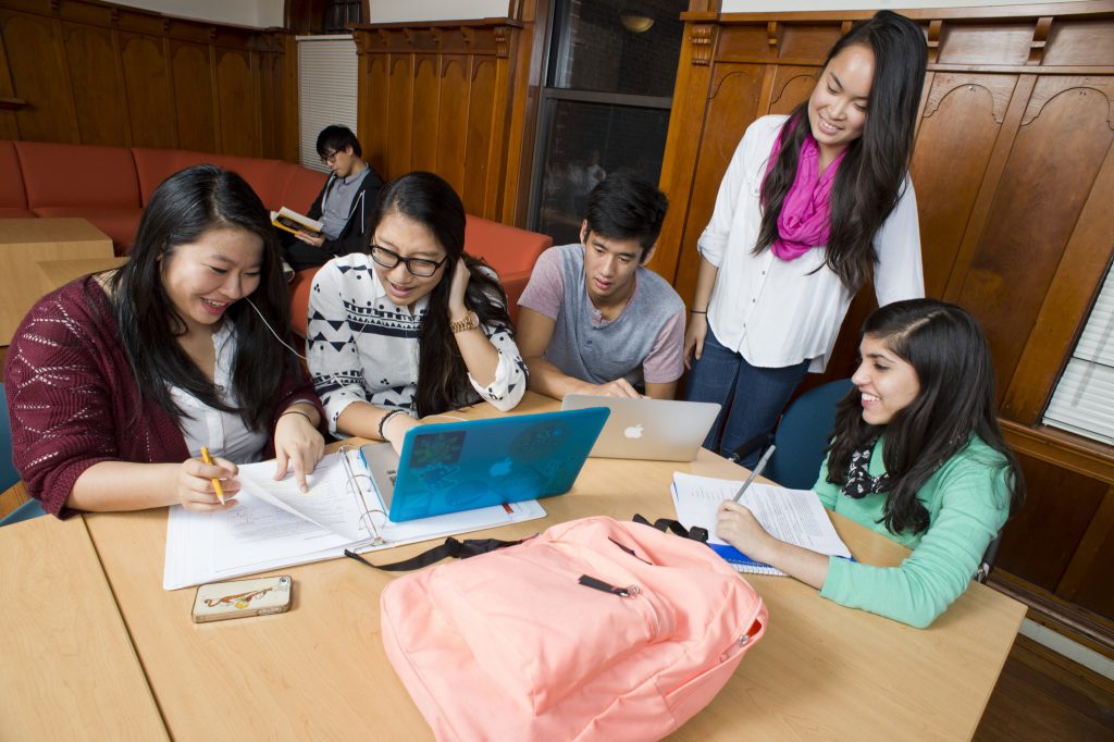 Image of students sitting around a table. They are writing on papers while one student has their laptop open.