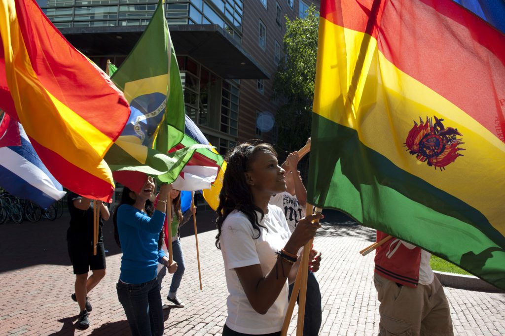 Students walking outside, carrying a variety of different country flags