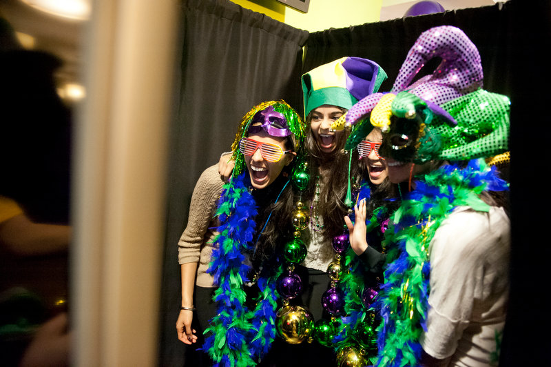 4 students pose for a picture. They are dressed in Mardi Gras attire, including hats, masks, necklaces and feather boas.