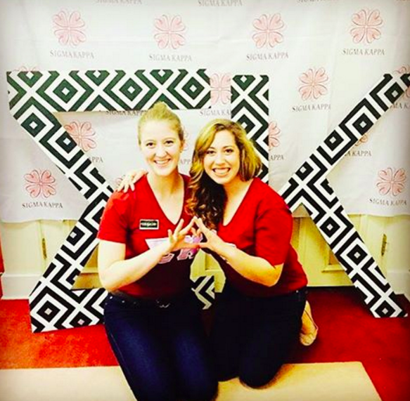 2 female students pose in front of greek letters